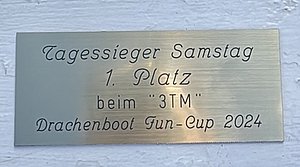 Eine metallene Plakette mit der Aufschrift: "Tagessieger Samstag, 1. Platz beim '3TM' Drachenboot Fun-Cup 2024".