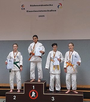 Vier junge Judoka stehen auf einem Siegertreppchen bei den Südwestdeutschen Einzelmeisterschaften 2025. Die Athletinnen tragen weiße Judokas und halten Urkunden in den Händen. Eine von ihnen, in der Mitte, hält eine Medaille. Die anderen haben orange, grüne und gelbe Gürtelschnallen.